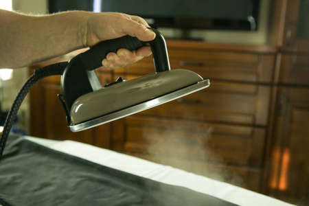 Homework. Close-up, woman ironing clothes with an iron on an ironing board after washing. The steam jet is clearly visible in the photo.の写真素材
