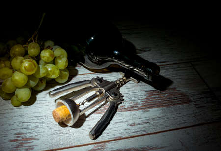 Autumn is the time for winemaking. Composition with a bottle of wine, a bunch of white grapes and a corkscrew on a wooden background.の写真素材
