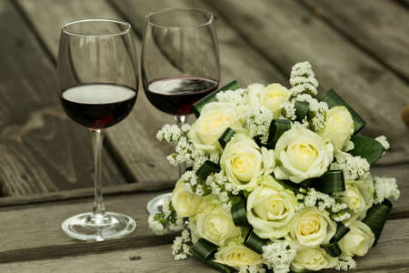 Wedding bouquet. Glasses with red wine and a wedding bouquet on the background of old wooden boards. The most important bouquet at the wedding is the bride's bouquet.の写真素材