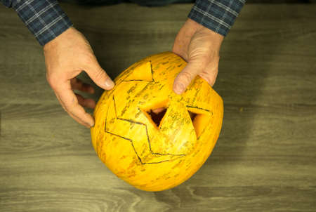 How to make Jack O'Lantern at home? Male hands with knife, leftovers of pumpkin on the kitchen table. Selective focus and bokeh.の写真素材