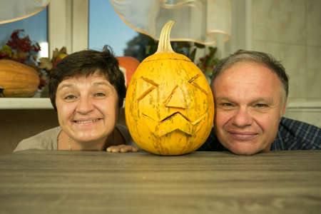 Making Jack O'Lantern at home. The pumpkin is ready. A man and a woman are satisfied with their work, laugh and joke.の写真素材