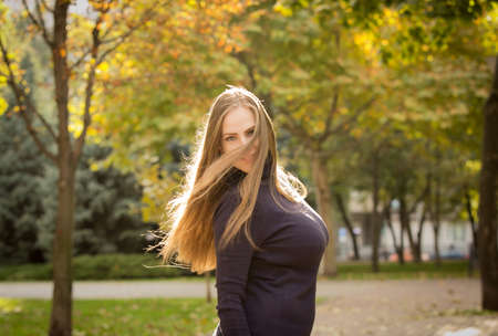 Beautiful young woman on a background of autumn trees. Emotion concept. Walk in the autumn park. Backlight shooting.の写真素材