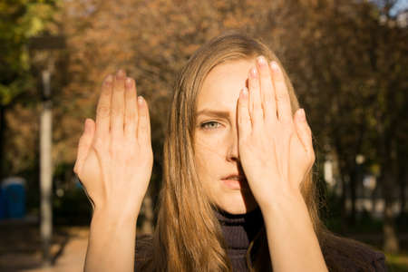 Beautiful young woman on a background of autumn trees. Emotion concept. The girl covers her face...