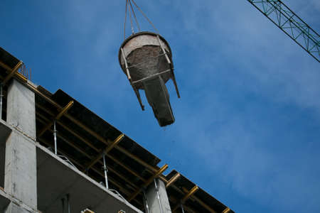 Building. Close-up of a construction crane that raises a container of concrete against a blue sky.の写真素材
