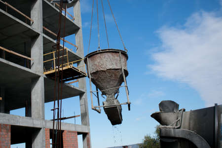Building. Close-up of a construction crane that raises a container of concrete against a blue sky.の写真素材