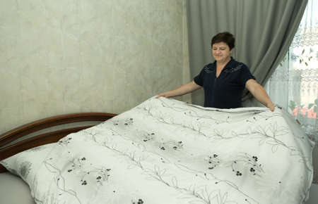Homework. A middle-aged woman covers fresh bedding.