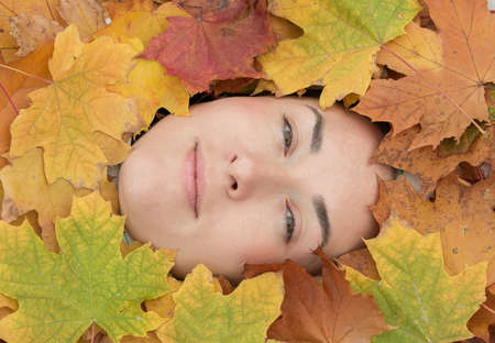 Fall. Portrait of a beautiful young woman in multicolored maple autumn leaves.の写真素材