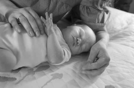 Mom's hands are holding the baby carefully. A serious and beautiful newborn baby is sleeping. The concept of maternal tenderness.の写真素材
