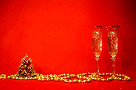 New Year and Christmas card on a red background. Two glasses of champagne, golden beads and a pyramid with red Christmas balls. Minimalism concept. Content for the designer.の写真素材