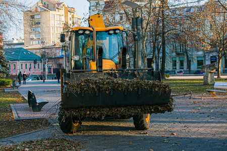 The municipal service is carrying out autumn works in the park. Cleaning fallen autumn leaves with an excavator and a truck in the city.の写真素材
