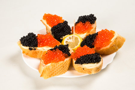 Sandwiches with red salmon caviar and black stougeon caviar on a white plate and white plate. Lemon slice in the center. View from above. Suitable for restaurant menus.の写真素材