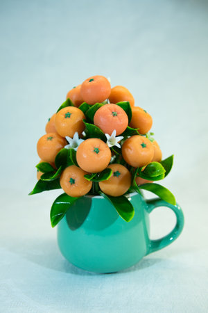 Gift bouquet of bright orange mandarin fruits and white flowers in a green cup. The bouquet is decorated with green leaves. Handmade tangerines from soap.の写真素材