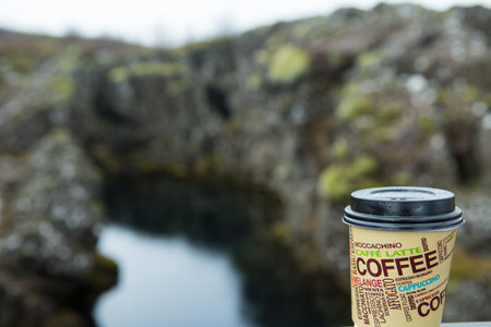 A glass of hot coffee against the backdrop of the harsh Icelandic landscape. Selective focus.のeditorial素材