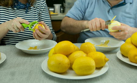 The process of making limoncello lemon liqueur at home. A man and a woman removes the zest from the...