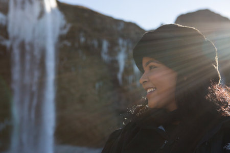 Hauyfoss waterfall, Iceland - 03.11.2018: Travel concept. Close up portrait of a happy African American woman walking near a waterfall in Iceland. Unforgettable journey.のeditorial素材