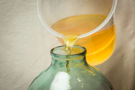 The process of making limoncello lemon liqueur at home. A man pours filtered alcohol infused with lemon zest into a ten-liter glass bottle.の写真素材