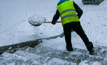Municipal services are engaged in snow removal after a snowfall. A worker removes snow from the street with a shovel.の写真素材
