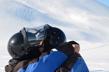A young woman and a man in helmets kiss after a quad bike ride in Svalbard. The couple are happy to have conquered the winter track.の写真素材