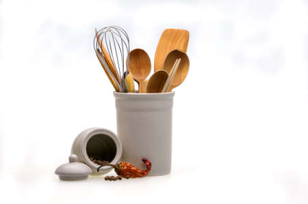 Wooden utensils for cooking in a white glass and red hot pepper. Kitchen spoons, scoops, forks...