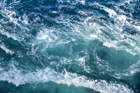 Abstract background. The waves of the sea water meet with underwater pointed rocks, forming...