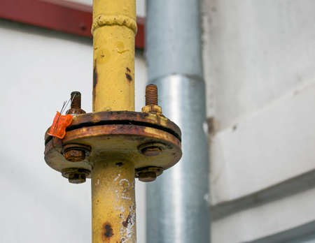 A yellow gas pipe with a coupler runs along the facade of a multi-story building. The house is...