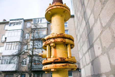 Yellow gas pipe with valve open close goes along the facade of a multi-storey building. House...