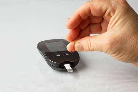 Analysis of blood sugar levels using a home glucometer. Female hand with a drop of blood and a...