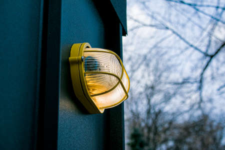 Modern street lamp on a stone wall. The lamp is on. The plafond is protected by a metal frame.の写真素材
