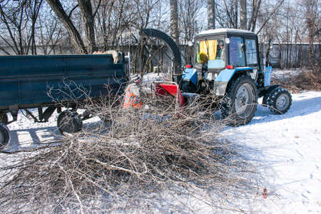 Dnepropetrovsk, Ukraine - 02.16.2021: Mobile shredder of dry branches and trees in a city park. Cleaning branches and small dry trees with a wood shredder. Workers recycle broken treesのeditorial素材