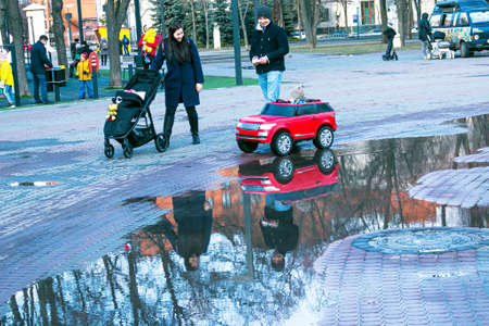 Dnepropetrovsk, Ukraine - 03.21.2021: Parents and children walk in the park after the rain. Reflections in puddles are visible in the bright sun.のeditorial素材