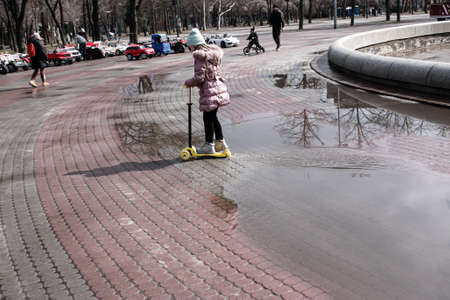 Dnepropetrovsk, Ukraine - 03.21.2021: Parents and children walk in the park after the rain. Reflections in puddles are visible in the bright sun.のeditorial素材