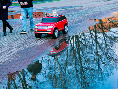 Dnepropetrovsk, Ukraine - 03.21.2021: Parents and children walk in the park after the rain. Reflections in puddles are visible in the bright sun.のeditorial素材