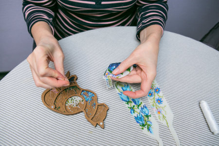 Weaving from beads. Close-up - a woman's hands are stringing beads on a thread, making jewelry. The woman is fond of weaving from beads.の写真素材