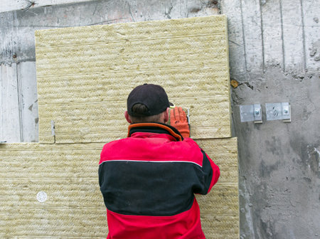 A man installs a layer of thermal insulation on the wall of the stairs outside - using mineral wool panels. The concept of repair and insulation of external structures.の写真素材