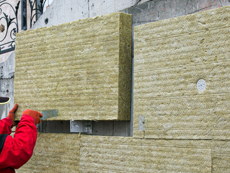 A man installs a layer of thermal insulation on the wall of the stairs outside - using mineral wool...