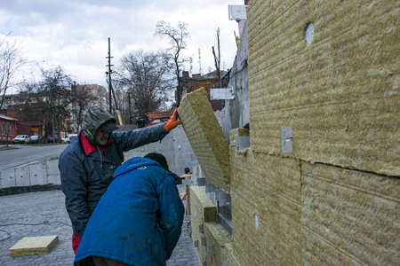 Dnepropetrovsk, Ukraine - 04/06/2021: A man installs a layer of thermal insulation in the form of mineral wool panels. Installation of isover blocks to a concrete wall.のeditorial素材