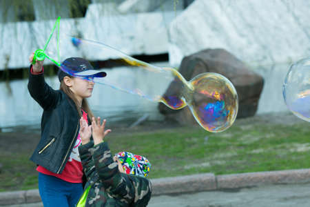 Dnepropetrovsk, Ukraine - 04.10.2021: Cheerful cute children blowing soap bubbles in a park in nature. Joyful emotions in a child, big bright soap balls.のeditorial素材