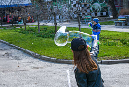 Dnepropetrovsk, Ukraine - 04.10.2021: Cheerful cute children blowing soap bubbles in a park in nature. Joyful emotions in a child, big bright soap balls.のeditorial素材