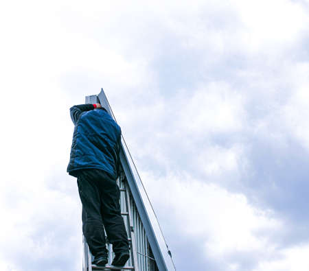 Repair of outdoor advertising banner mechanism on a cloudy day. The specialist climbs the stairs to...