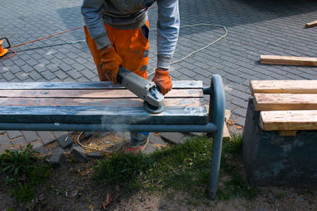 Sanding wood, cleaning paint of an old bench. Preparation for painting. Municipal services are...