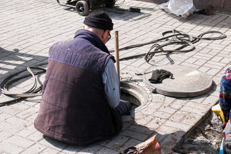 Dnepropetrovsk, Ukraine - 03.26.2021: Water utility workers open an old manhole and replace old rusty pipes with new ones.のeditorial素材