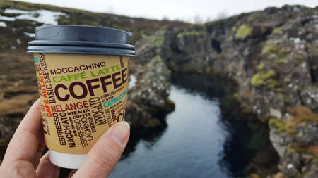 Iceland - 03.15.2018: Glass with coffee on the background of the Icelandic river. A female hand...