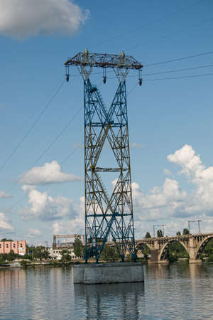 High-voltage pylons of power lines on the river. Metal pylons of high-voltage power line on concrete base.の写真素材