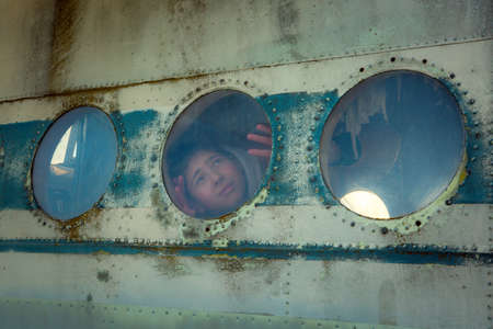 A young man on board an old abandoned Soviet plane. The guy looks out the window.の写真素材