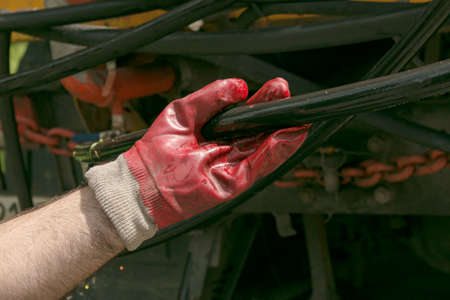 A man's hand in a rubber glove holds a watering hose. The hose must be secured to the sprinkler.