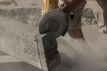 The process of laying sidewalk curb. A worker cuts a concrete block with a circular saw. A lot of dust.の写真素材