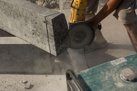 The process of laying sidewalk curb. A worker cuts a concrete block with a circular saw. A lot of dust.の写真素材
