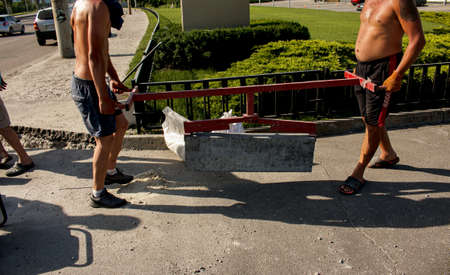 Dnepropetrovsk, Ukraine - 06.26.2021: The process of laying sidewalk curb. Workers place a deflected piece of concrete curb into a prepared recess or trench.のeditorial素材