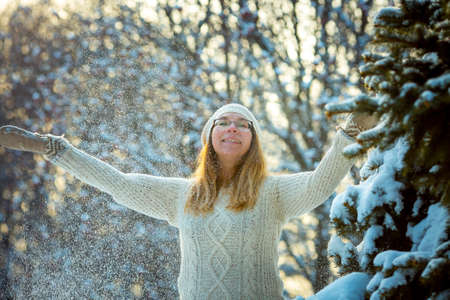 Happy woman plays with a snow in sunny winter day. Girl enjoys winter, frosty day. Playing with snow on winter holidays, a woman throws white, loose snow into the air. Walk in winter forest.の写真素材