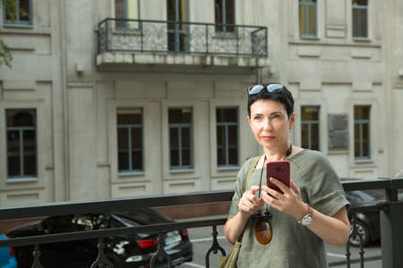 Attractive middle-aged woman with a phone in the city. The woman is emotionally talking on the...
